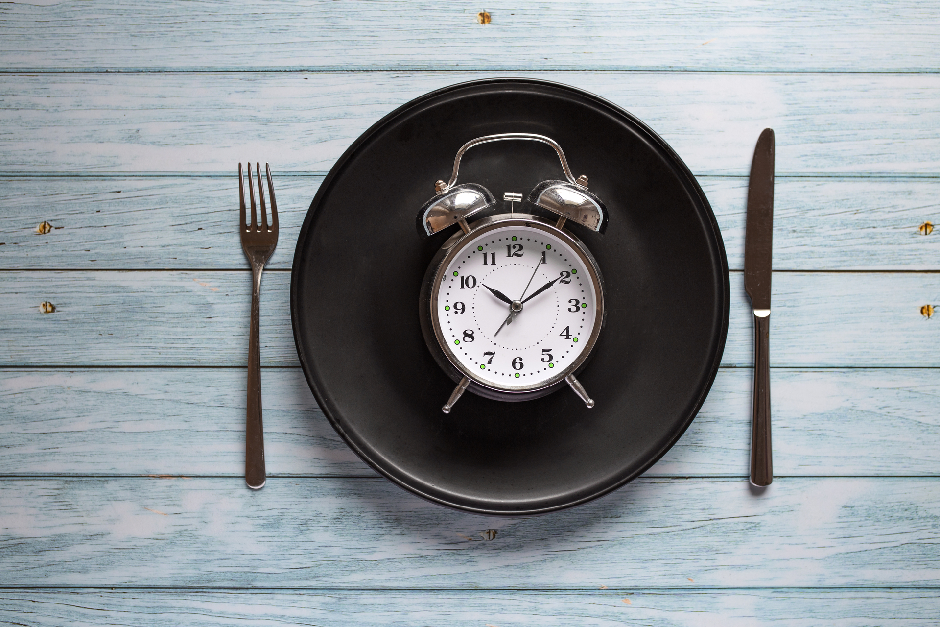 Meal planning for diet concept , Intermittent fasting concept with clock on plate, fork and knife on wooden table, Clock on plate with fork and knife, intermittent fasting, meal plan, weight loss