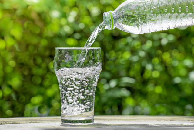 Pour water from a plastic bottle into a glass. The background of the plants in the garden. soft focus.