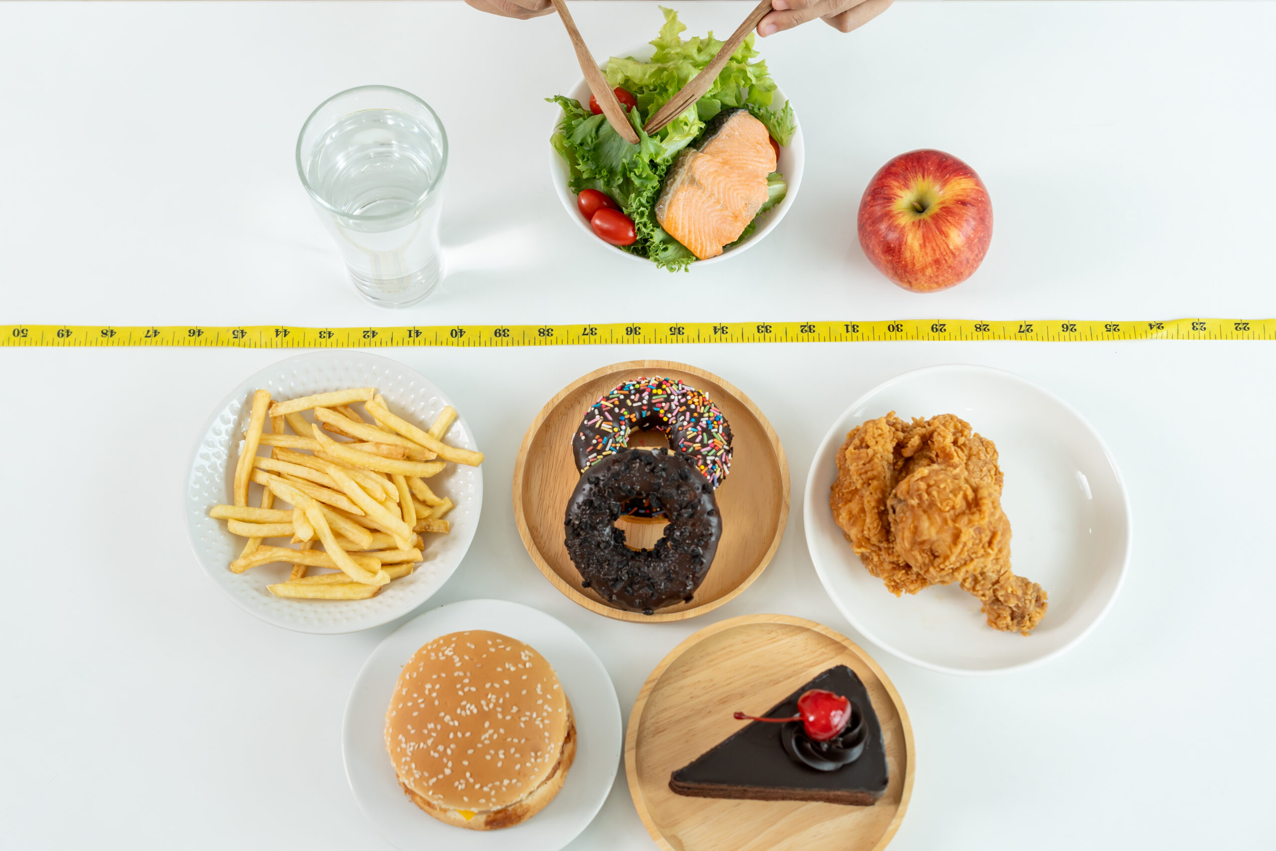 Woman choose healthy food for diet. Healthy food and fatty food separated on table with measuring tape. Lose weight, balance, control, reduce fat, low calorie, routine, exercise, body shape.